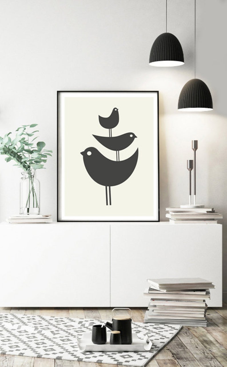 Pu&ograve; includere: Una stampa d'arte minimalista in bianco e nero con tre uccelli stilizzati appollaiati su un ramo. La stampa &egrave; incorniciata in una cornice nera e appesa a una parete bianca.