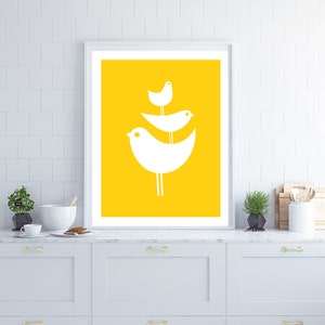 May include: A framed print with a yellow background and three white stylized birds perched on a branch. The birds are arranged in a triangular shape, with the largest bird at the bottom and the smallest bird at the top.