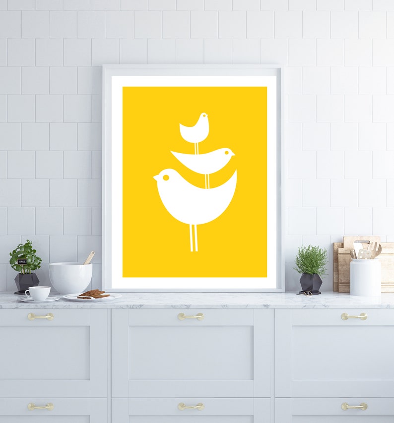 May include: A framed print with a yellow background and three white stylized birds perched on a branch. The birds are arranged in a triangular shape, with the largest bird at the bottom and the smallest bird at the top.