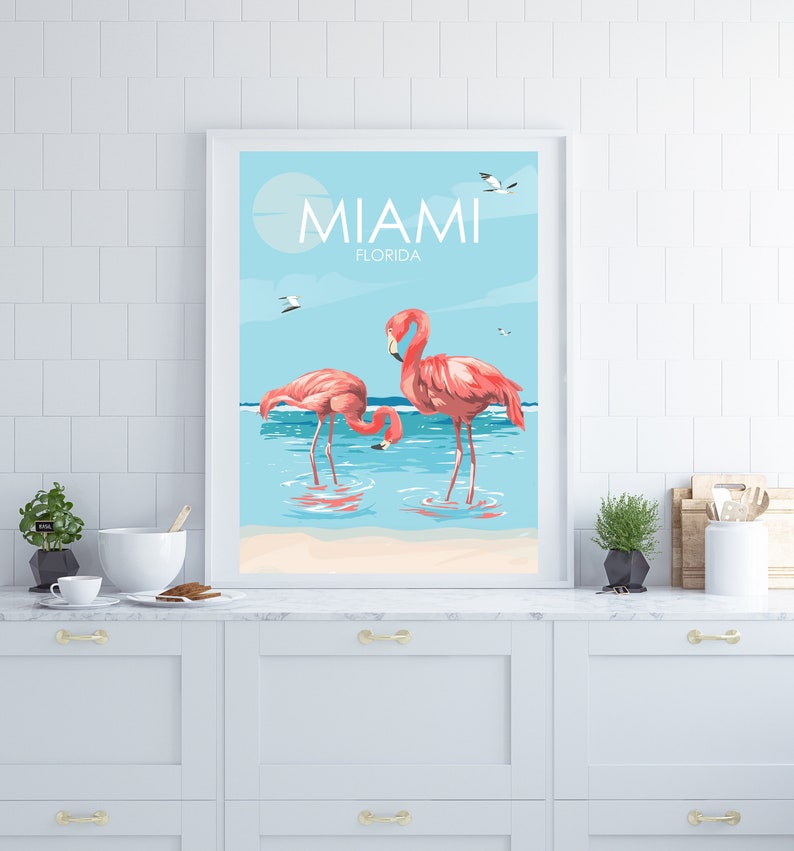 K&ouml;nnte beinhalten: Ein gerahmtes Poster mit blauem und wei&szlig;em Hintergrund, auf dem zwei rosa Flamingos im Wasser stehen. Das Poster zeigt oben "Miami, Florida" an.