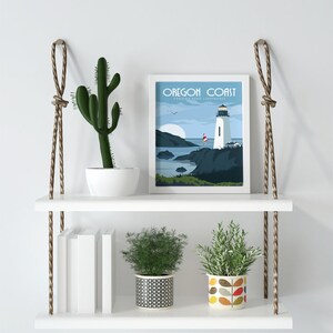 May include: White floating shelves with rope hangers, featuring a cactus, two potted plants, a stack of books, and a framed print of a lighthouse with the text "Oregon Coast - Tillamook Head Lighthouse".
