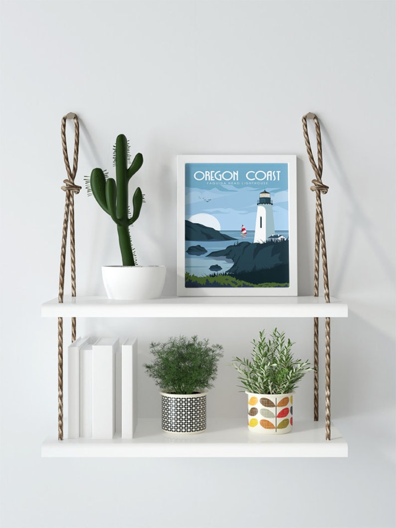 May include: White floating shelves with rope hangers, featuring a cactus, two potted plants, a stack of books, and a framed print of a lighthouse with the text "Oregon Coast - Tillamook Head Lighthouse".