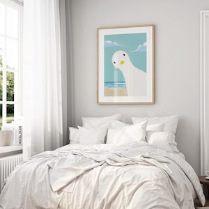 Puede incluir: Una cama blanca con ropa de cama y almohadas blancas. Un estampado enmarcado de un p&aacute;jaro blanco con un pico amarillo sobre un cielo azul y una escena de playa cuelga en la pared detr&aacute;s de la cama.