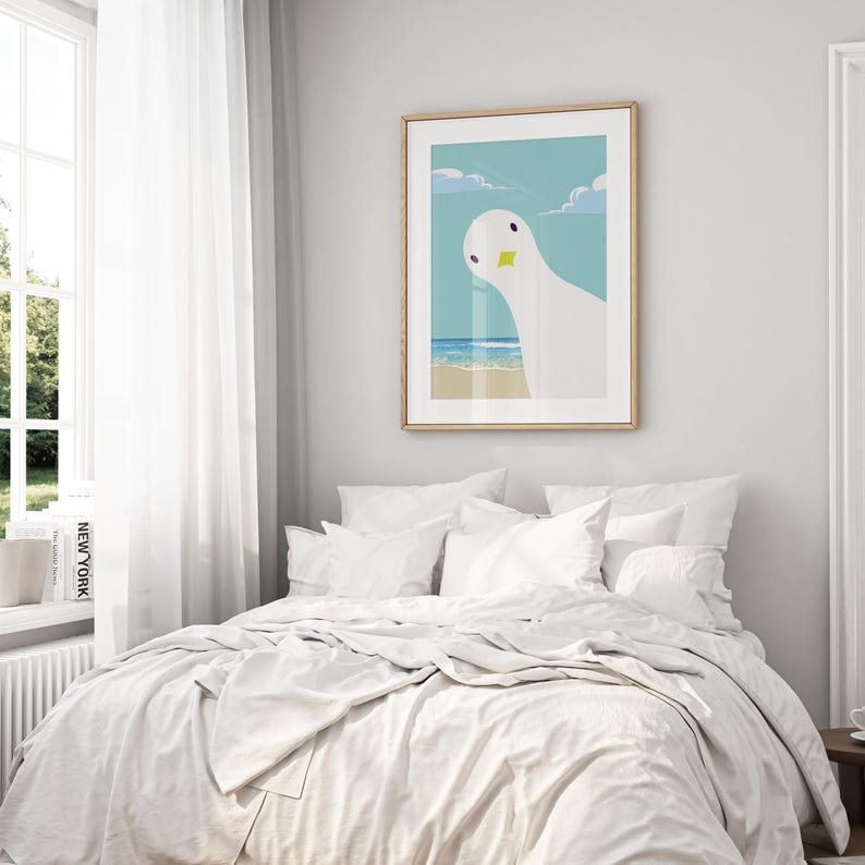 Puede incluir: Una cama blanca con ropa de cama y almohadas blancas. Un estampado enmarcado de un p&aacute;jaro blanco con un pico amarillo sobre un cielo azul y una escena de playa cuelga en la pared detr&aacute;s de la cama.