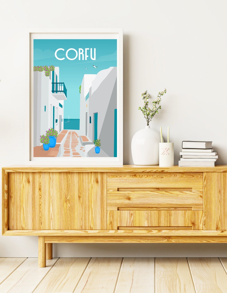 May include: A white framed print with a blue and white illustration of a street in Corfu, Greece. The print is hanging on a white wall above a wooden cabinet.