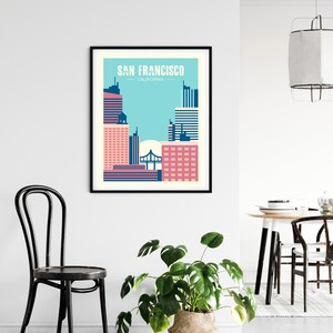 May include: A black framed poster with a graphic design of the San Francisco skyline in pink, blue, and white. The text "SAN FRANCISCO - CALIFORNIA" is at the top of the poster.