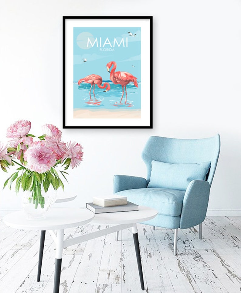 K&ouml;nnte beinhalten: Ein Poster mit blauem Hintergrund und wei&szlig;en Wolken. Der Text "MIAMI FLORIDA" befindet sich oben auf dem Poster. Zwei rosafarbene Flamingos stehen im Wasser.