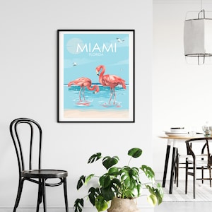 K&ouml;nnte beinhalten: Ein Poster mit blauem Hintergrund und dem Text "Miami, Florida" in Wei&szlig;. Zwei rosafarbene Flamingos stehen im Wasser mit einem wei&szlig;en Sandstrand im Hintergrund.