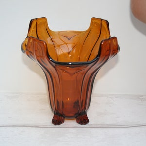 May include: Amber glass vase with a wide, flared opening and a fluted body. The vase has a square base with four feet.