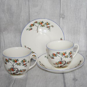 May include: A set of two white teacups and saucers with a blue rim and a floral design featuring orange and green fruit on a tree branch.