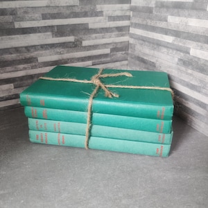 Könnte beinhalten: Ein Stapel Vintage-Bücher in Grüntönen, mit Bindfaden zusammengebunden. Die Bücher haben rote Schrift auf den Buchrücken. Die Bücher sind auf einer grauen Oberfläche gestapelt, mit einer grau-weißen Backsteinmauer im Hintergrund.