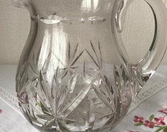 Puede incluir: Una jarra de vidrio transparente con un diseño de vidrio cortado. La jarra tiene un cuerpo redondo y un asa.