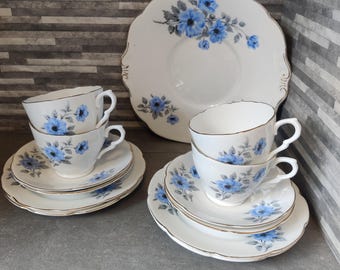 Könnte beinhalten: Ein Vintage-Teeservice mit weißen Porzellantassen, Untertassen und einem Servierteller. Jedes Stück ist mit einem zarten blauen Blumenmuster und goldenen Verzierungen versehen. Das Set enthält zwei Tassen- und Untertassenpaare sowie einen großen Servierteller.