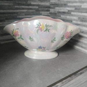 Puede incluir: Un tazón de cerámica blanca con un borde rosa y diseños florales. El tazón tiene un borde festoneado y una base de pedestal.