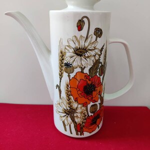 May include: White ceramic coffee pot with a floral design featuring red poppies, white daisies, and wheat stalks. The pot has a lid and a handle.