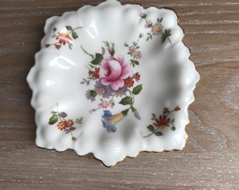 May include: A white porcelain dish with a scalloped edge and a floral design. The flowers are pink, purple, and yellow, and the leaves are green.
