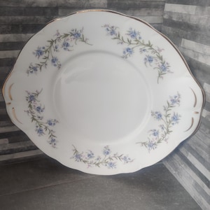 Peut inclure: Assiette de service en porcelaine blanche avec bord festonné et bordure dorée. Un motif floral bleu délicat décore le bord. L'assiette a deux poignées et convient pour servir des gâteaux ou d'autres desserts.