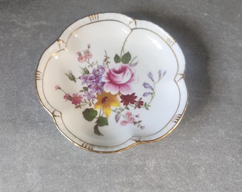 May include: A white porcelain dish with a scalloped edge and a gold trim. The dish features a floral design with pink, yellow, and purple flowers.
