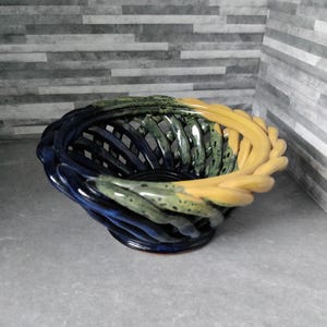 May include: A ceramic basket with a woven design. The basket has a colour gradient, shifting from navy blue to green and then to yellow. The basket is a decorative item, suitable for display.