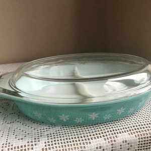 May include: A turquoise blue casserole dish with a white snowflake design and a clear glass lid. The dish is divided into three sections.