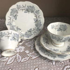 May include: A vintage tea set with a silver and white leaf pattern. The set includes a teapot, a cup, a saucer, and a plate.
