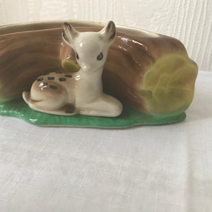 May include: A ceramic planter shaped like a log with a fawn lying on top. The planter is painted brown, green, and yellow.