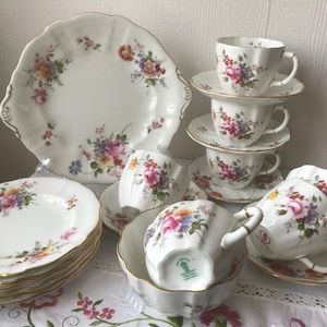 May include: A set of vintage floral teacups and saucers with a matching cake plate and serving platter. The china features a delicate floral pattern in shades of pink, yellow, and blue.