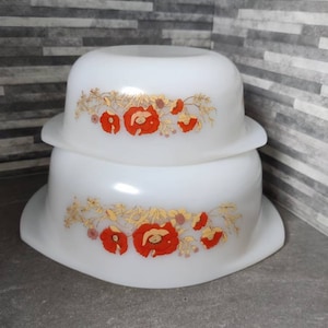 May include: Two white ceramic bowls with a floral design. The bowls have a white background with a gold and red floral pattern. The bowls are stacked on top of each other.
