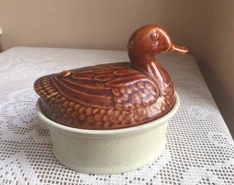 Könnte beinhalten: Eine braune Keramik-Schale in Form einer Ente mit einem weißen Sockel. Die Ente hat ein detailliertes Design und eine glänzende Oberfläche.