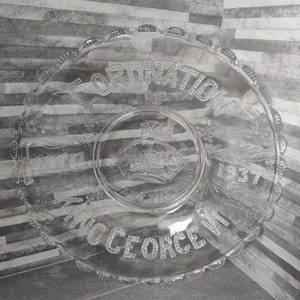 May include: A clear glass plate with a scalloped edge. The plate has a raised design of a crown and the words "Coronation of King George VI 1937".