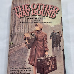 May include: Vintage paperback book titled "The Other Way Round" by Judith Kerr. The cover art features a woman in a brown coat carrying luggage, with text that reads "When Hitler Stole Pink Rabbit". The book's theme is about the war.
