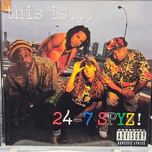 May include: CD case featuring the album cover for "this is..." by 24-7 Spyz. The cover art shows four band members in front of a city backdrop. The band's name is prominently displayed with the Parental Advisory label.