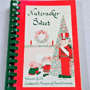 May include: A spiral-bound cookbook titled Nutcracker Sweet with a bright red border. The cover features a Christmas tree, a nutcracker, and two children by a fireplace. Text includes Women's Guild and Jacksonville Museum of Arts & Sciences.