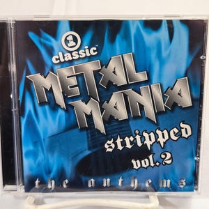 May include: A CD case for "Metal Mania Stripped Vol. 2: The Anthems." The cover features a blue flame design with the words "Metal Mania" in a silver, bold font. The CD case is clear plastic.