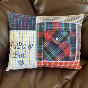 May include: A patchwork pillow with a blue, red, and yellow plaid design. The pillow has a pocket on the front and is embroidered with the text "PaPaw Bob" and a heart.