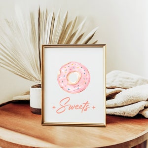Puede incluir: Una impresión enmarcada con una dona rosa con chispas de colores y la palabra "Sweets" en escritura rosa.