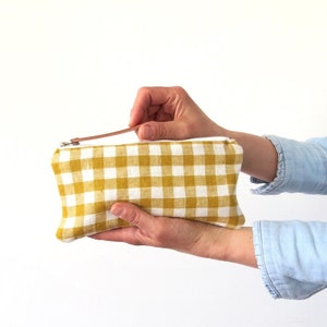 A cute linen pencil case, in mustard yellow and off white. The pouch is being hold on one hand, and opened with the other one.