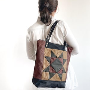 May include: A patchwork tote bag with a star design. The bag features a combination of brown, tan, and black fabrics. It has black leather handles and a zip closure. The bag is carried over the shoulder.