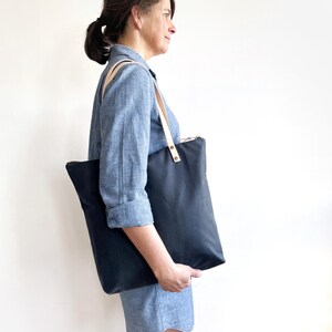 A woman wears the bag with the handles on her shoulder.