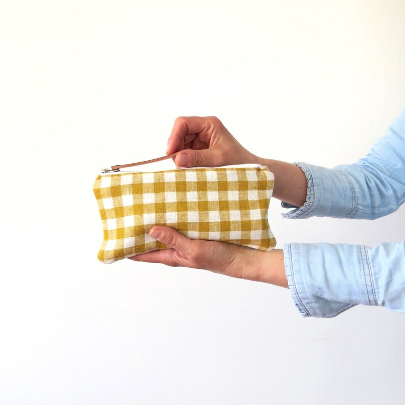 A cute linen pencil case, in mustard yellow and off white. The pouch is being hold on one hand, and opened with the other one.