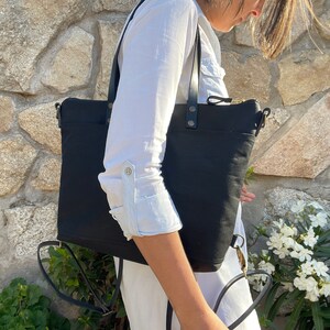 A woman wears the bag as a tote bag with the leather straps on her shoulder.