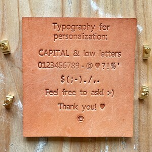 A leather swatch in natural colour, engraved with the characters available for personalization.