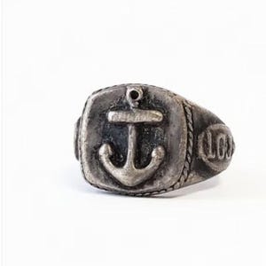May include: A silver-toned metal ring featuring a prominent anchor emblem embossed on the square face. The band is detailed with a rope-like texture along the edges and includes the letters LCJ engraved on the side of the ring shank.