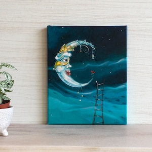 Puede incluir: Una pintura caprichosa muestra una luna creciente sonriente con una máscara de carnaval sobre un cielo nocturno azul oscuro. Una escalera conduce a la luna. La obra de arte sobre lienzo presenta estrellas y nubes.