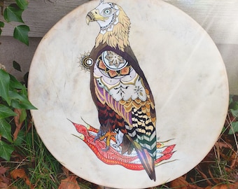 May include: A hand-painted drum featuring a detailed illustration of an eagle with intricate patterns and colours. The eagle is perched on a red and orange design.