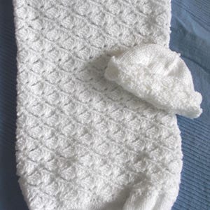 May include: White crocheted baby blanket and hat set. The blanket is made with a textured stitch and has a scalloped edge. The hat is a simple beanie style.