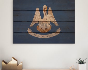 May include: A wooden wall art piece featuring the Louisiana state flag. The flag design includes a pelican with a nest and the text "UNION JUSTICE CONFIDENCE" on a blue background. The artwork is displayed on a white wall.