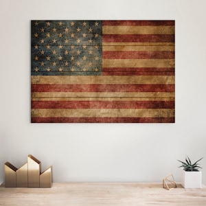 May include: A distressed American flag design on a wooden panel. The flag features 50 gold stars on a blue background and red and tan stripes. The artwork is mounted on a white wall above a wooden surface.