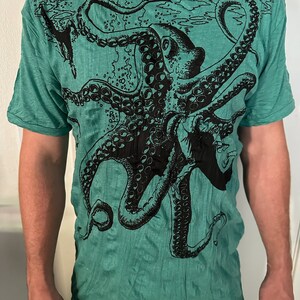 May include: A short-sleeved t-shirt in a vibrant teal green color featuring a large, detailed black ink-style graphic print of an octopus. The design covers the front of the shirt, showcasing the creature's tentacles and suction cups.
