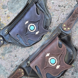 May include: Two dark brown leather fanny packs featuring a zippered main compartment and a front pocket with a decorative cutout design. Each bag is centered with a round turquoise stone inlay and accented with brass rivets and stitched leather straps.